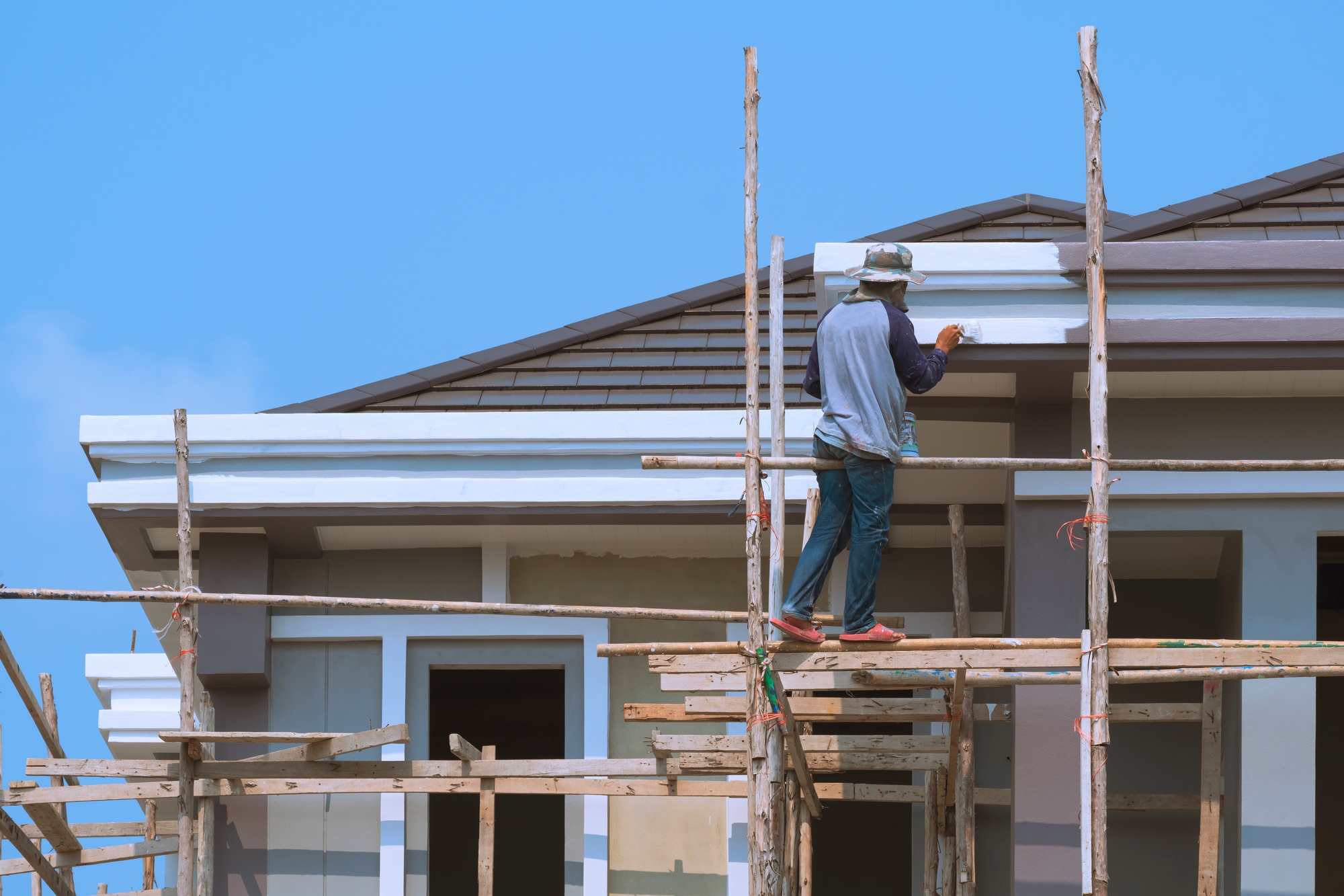 Asian builder worker on wooden scaffolding is painting roof structure of modern house