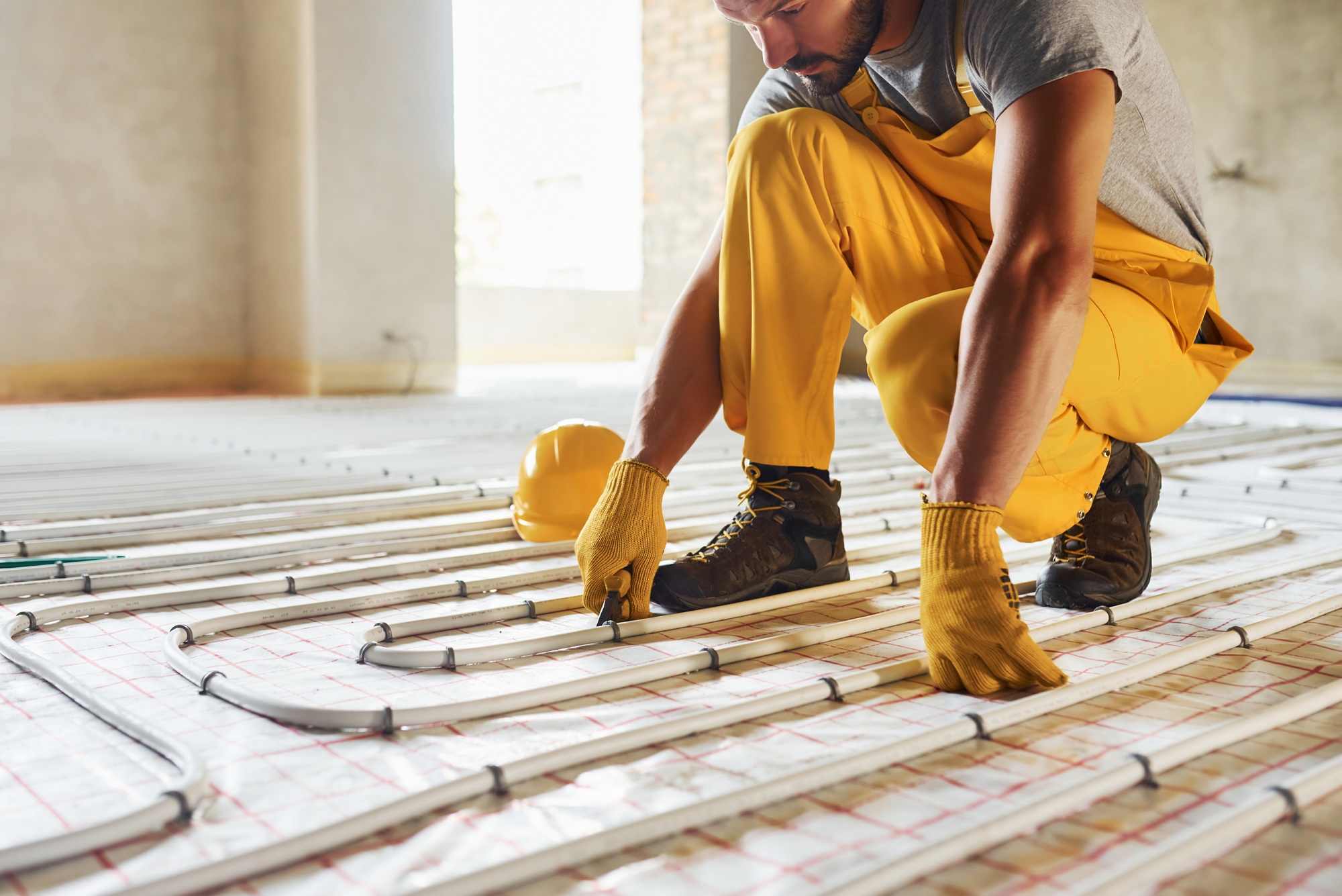 Many of pipes. Worker in yellow colored uniform installing underfloor heating system
