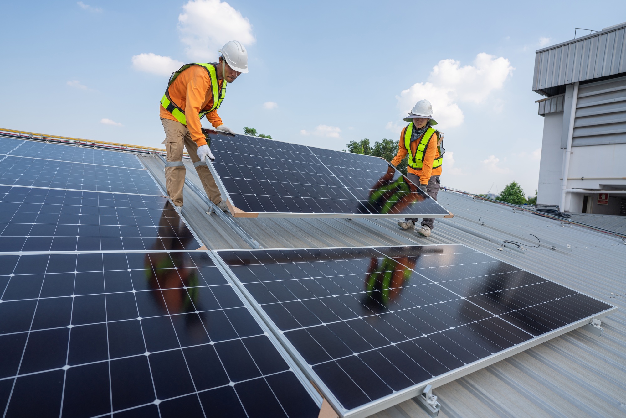 Men technicians carrying photovoltaic solar moduls on roof.